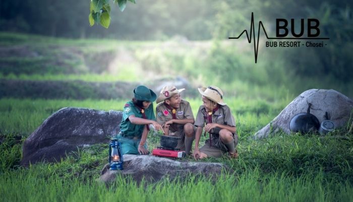 アウトドアな恰好をした子供3人が自然の中で楽しそうに話している様子